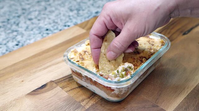 hand dipping tortilla chip into baked seven layer mexican bean dip
