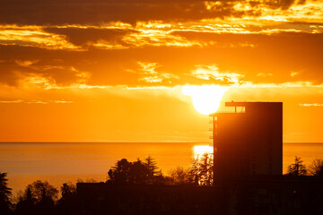 A stunning sunset over the sea with a bright orange sky and a hotel complex on the shore. The image showcases resort properties, perfect for travel and vacation-related themes. © NastyaPhoto