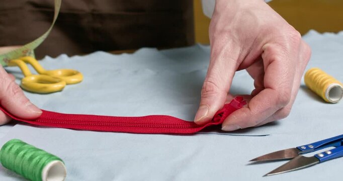 Man tailor carefully places bright red zipper against fabric checking length before sewing. Male puts zipper on fabric surface confirming accurate alignment