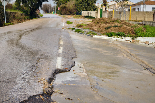 View of a cracked road surface showing signs of wear and tear, with greenery peeking through the edges, Setenil de las Bodegas, Andalusia, Spain.