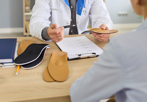 Doctor orthopedist and patient discuss orthopedic insole during foot health consultation in hospital. Hand of podiatrist holding leather orthotic insert for feet arch support, flatfoot treatment
