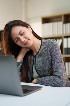 Businesswoman experiencing discomfort and neck pain, rubbing her shoulder and closing her eyes while feeling overworked and stressed from prolonged computer usage in the office