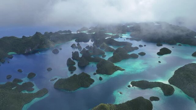 Cinematic aerial drone view of Wayag, Raja Ampat, Indonesia, with soft low clouds drifting above the iconic limestone karst islands. Turquoise lagoons and emerald tropical waters contrast beautifully 
