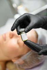 Fototapeta premium Gloved hand holding serum bottle over woman in salon