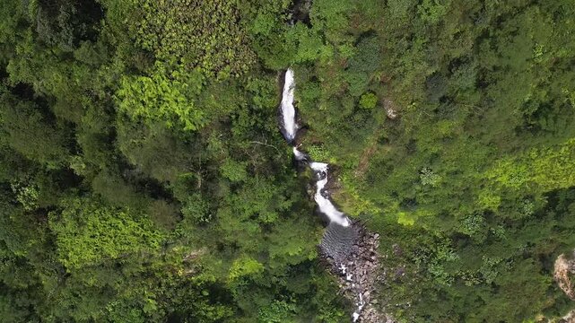 Aerial drone video showing Curug Cikawah waterfall cutting through lush jungle terrain in Bogor, West Java, Indonesia. Untouched rainforest environment and tropical ecosystem.