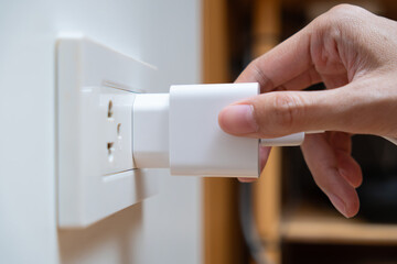 Close up of woman a hand connecting a white power adapter to a wall socket. Concept of charging devices and electricity consumption.