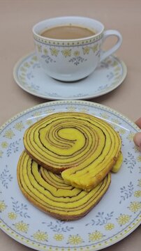 A cup of coffee with milk and a plate of lapis legit cake, one of Indonesia's traditional cakes, enjoying coffee in the morning.
