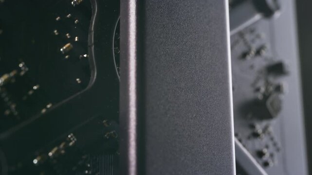Macro shot inside a dark aluminium computer, low angle of SSD solid-state drive, motherboard, capacitors and components. Dramatic lighting, metallic, matten modern, reflective interior hardware.