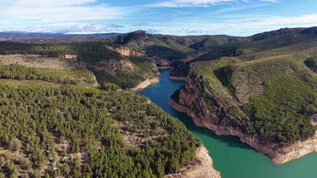 Cinematic orbit aerial around a turquoise lake carved through a limestone canyon, revealing forested slopes, stratified cliffs and sinuous shoreline contours