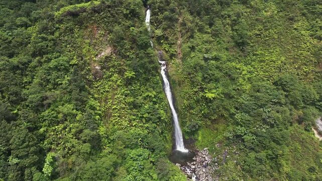 Drone shot of Curug Cikawah waterfall descending dramatically through lush rainforest cliffs in Bogor, Indonesia. Natural tropical scenery ideal for environmental, travel, and adventure.