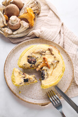 Quiche with chanterelles, oyster mushrooms, champignons, and cheese, piece of quiche cut off for eating on plate.