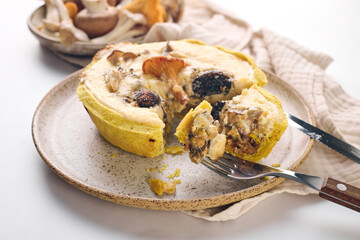 Quiche with chanterelles, oyster mushrooms, champignons, and cheese, piece of quiche cut off for eating on plate.