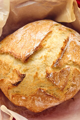 Golden sourdough bread with cracked crust in red ceramic Dutch oven, lined with parchment paper. Perfect for culinary, baking, and food photography projects.