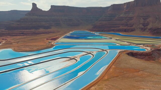 Aerial view of vibrant turquoise evaporation ponds contrasting with the stark red rock landscape, creating a surreal vista, Moab, Utah, United States.