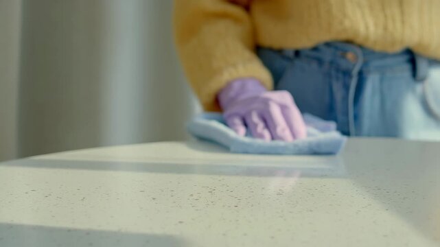 close up of woman hand in purple glove wiping white table with blue cloth
