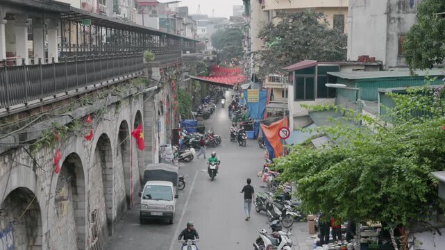 People on motorbikes navigate a busy street in Hanoi, Vietnam, near the Long Bien Bridge. The bridge is a landmark, and the street is a bustling hub of activity.
