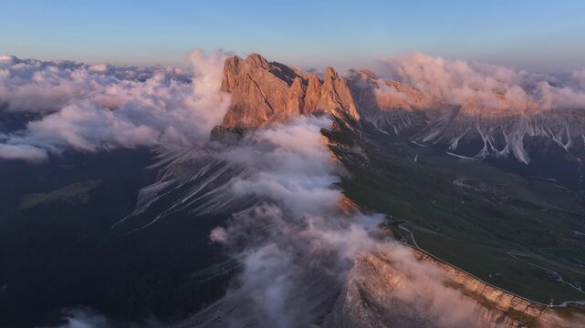 Aerial view of the rugged Seceda mountain peaks piercing through a sea of clouds, showcasing the dramatic landscape, Seceda, Trentino-South Tyrol, Italy.