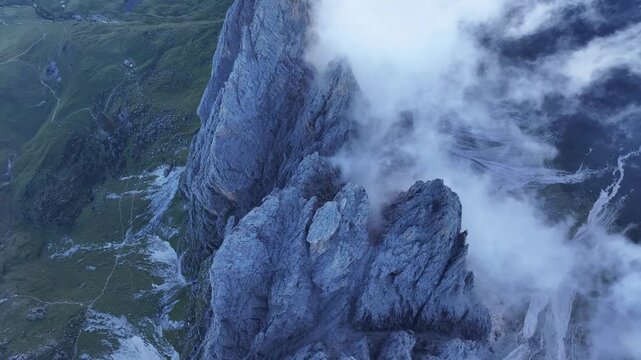 Aerial view of rugged mountain peaks shrouded in mist, contrasting with patches of green vegetation, in Seceda, Trentino-South Tyrol, Italy.