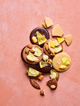 Various chocolate pieces including dark, milk, and caramel are topped with almonds, hazelnuts, dried orange, apple, mango, and sea salt