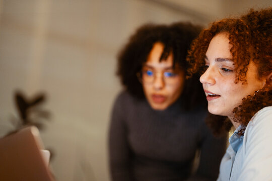 Two young women collaborate on a project, looking intently at a laptop screen.