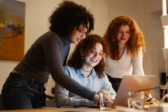 Three young women collaborate on a project, gathered around a laptop, sharing ideas and working together in a warm, inviting space.