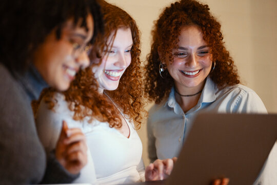 Three young women share a laugh while looking at a laptop screen together, enjoying a moment of connection and shared experience.