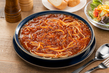 食卓に置かれたミートソースのスープパスタとパン