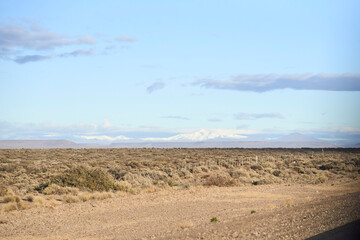 Traveling through the province of Neuquen, Argentina, during winter. Low vegetation in the foreground, snow-capped mountains in the background.
