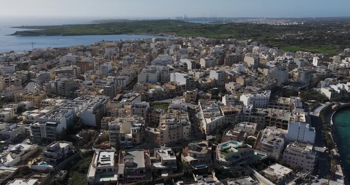 Aerial view of buildings in Marsaskala, where the architecture contrasts with the blue sea, creating a captivating scene, Marsaskala, Wied il-Ghajn, Malta.