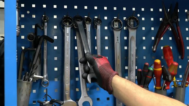 Professional technician hand selecting a large metal wrench from an organized blue pegboard storage rack in an industrial manufacturing factory plant workshop