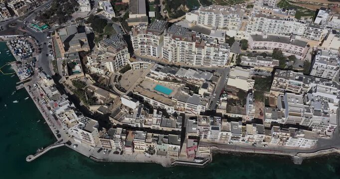 Aerial view of buildings and a pool, showcasing the contrast between the buildings and the clear blue water, Marsaskala, Wied il-Ghajn, Malta.