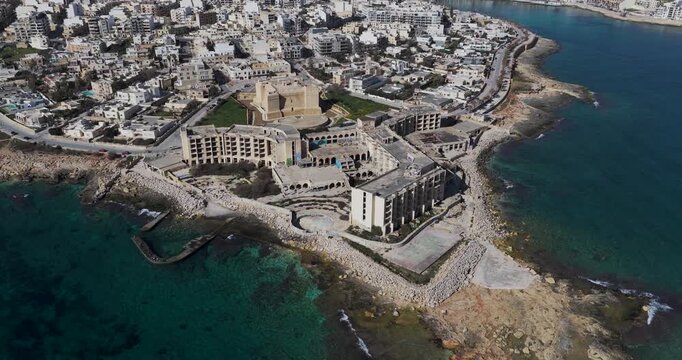 Aerial view of Fort St. Thomas with buildings and rocky coastlines, displaying the contrast between urban architecture and natural beauty, Marsaskala, Wied il-Ghajn, Malta.