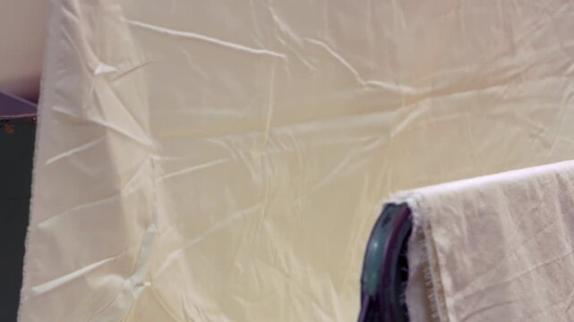 White fabric entering a large industrial textile machine during manufacturing. Automated equipment processes cloth materials before they continue through the textile production line.