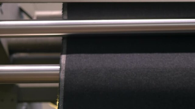 Blue textile fabrics moving through large industrial rollers inside a textile factory. Fabric treatment process where cloth is guided through machines during production