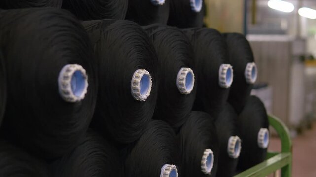 Large rolls of black fabric stacked in a textile factory warehouse. Textile materials ready for distribution and further garment manufacturing processes.