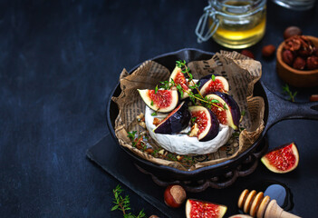 Camembert or brie cheese with fresh figs walnuts  and honey on iron frying pan, over dark background