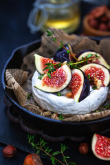 Camembert or brie cheese with fresh figs walnuts  and honey on iron frying pan, over dark background
