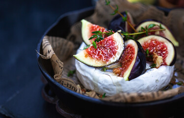 Camembert or brie cheese with fresh figs walnuts  and honey on iron frying pan, over dark background