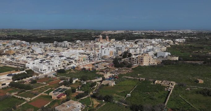 Aerial view of buildings and a church standing amidst the landscape, contrasting the urban structures with the surrounding greenery, Dingli, Malta.