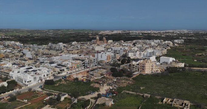 Aerial view of the town with the Dingli Parish Church surrounded by buildings and green fields under the bright sky, Dingli, Malta.
