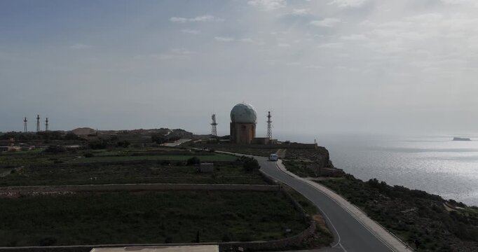 Aerial view of Dingli Radar Station, a spherical structure and towers, standing on a cliff overlooking the sea, with a road winding beside it, Dingli, Malta.