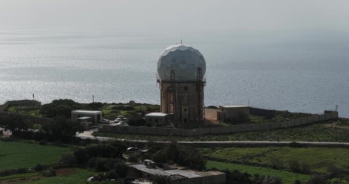 Aerial view of the Dingli Radar Station, a spherical structure with a wall, and greenery contrasting against the blue sea, Dingli, Dingli Radar, Malta.