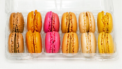 Colourful traditional French macaroons cakes inside plastic box isolated on white