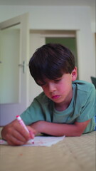Naklejka premium Boy lying on floor drawing with red marker, focused expression while creating artwork on paper in quiet indoor home setting