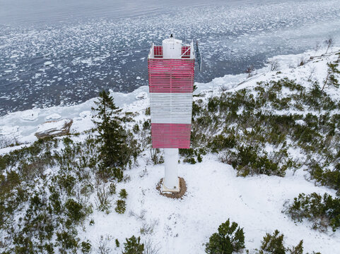 Aerial drone view of a red and white striped lighthouse tower on the snowy coast of Pakri Island in Estonia