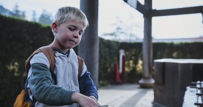 Little boy washing his face with water at Japanese shrine area - slow motion