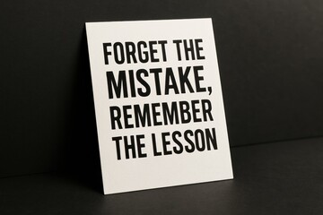 Minimalist stock photo featuring a white card displaying "Forget the mistake, remember the lesson" in bold black letters. Suitable for motivational, educational or business content.