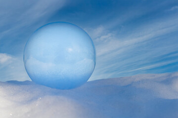 Frozen Soap Bubble Resting on Snow with Beautiful Blue Sky