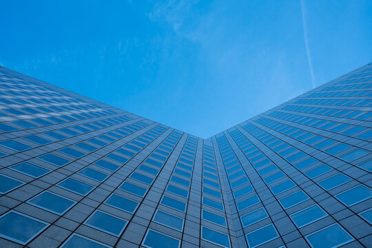 Looking up at a glass skyscraper against bright blue sky with symmetric lines and sharp perspective creating a clean abstract background