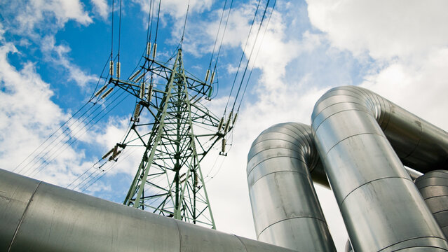 a pipeline and a power transmission tower against a blue sky and clouds